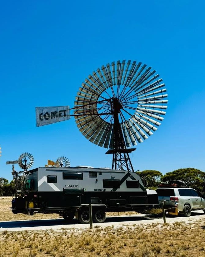 An Everest Avalanche caravan and tow vehicle parked beside a Comet windmill