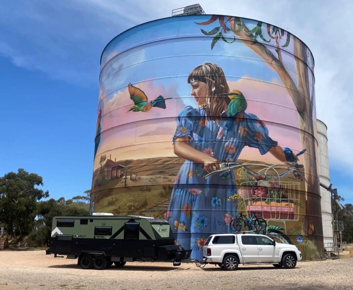 An Everest caravan and tow vehicle parked at a painted silo
